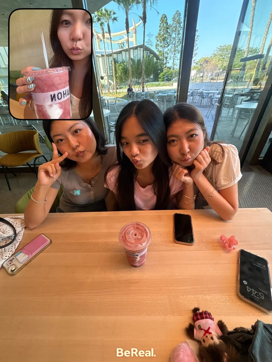 Three friends making faces at an outdoor campus table, sharing a smoothie