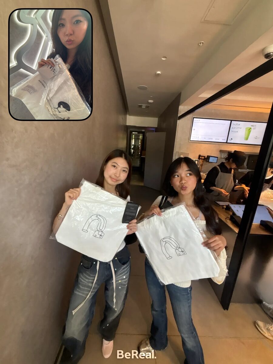 Two friends holding matching tote bags in a cafe hallway