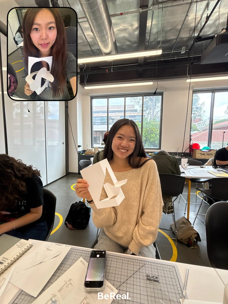 Smiling while holding a folded paper geometric model in a design studio