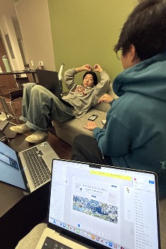 Late-night work session — one person mid-laugh on a couch, another looking at a laptop with a kanban board open