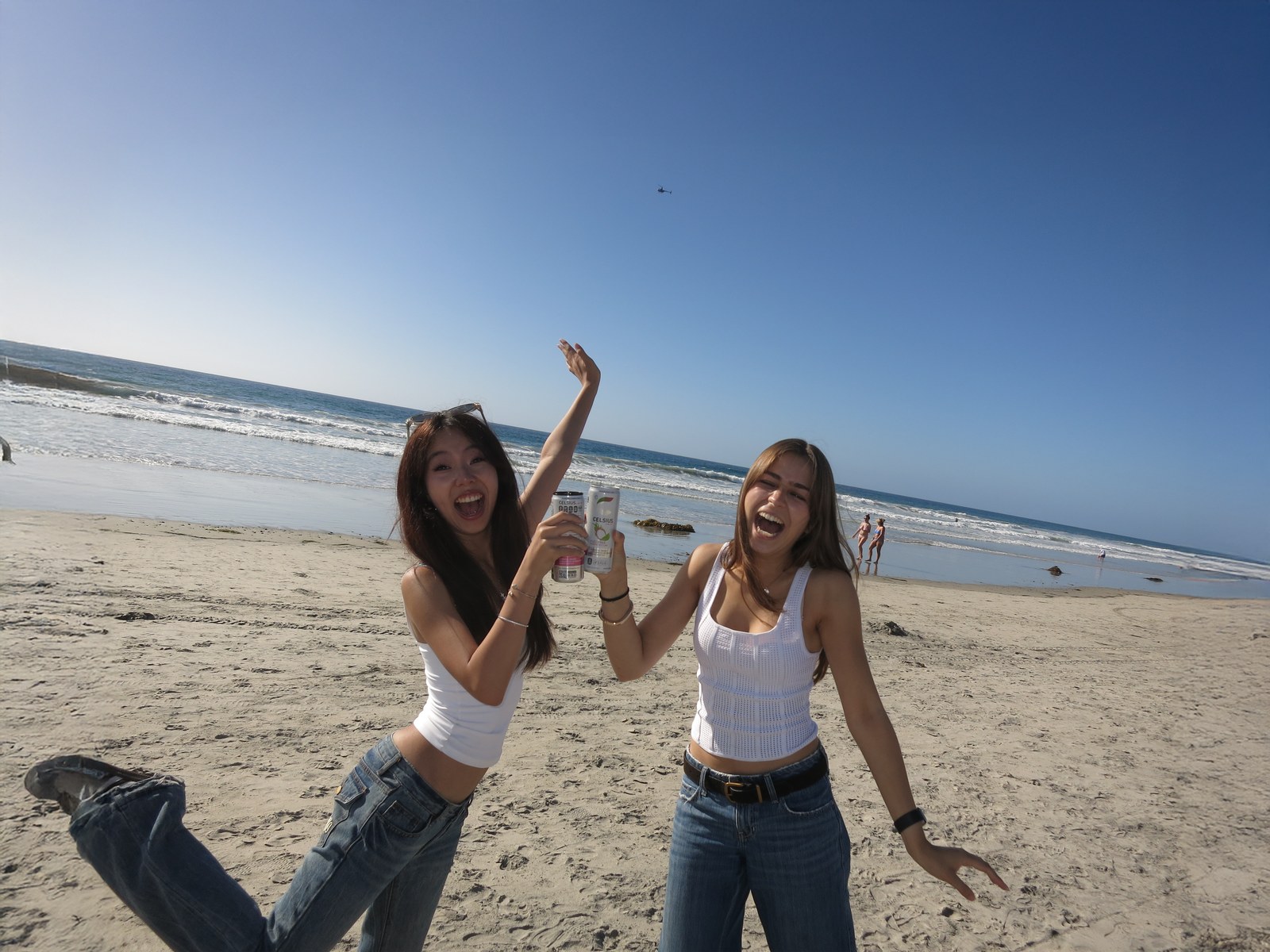 Two friends cheering on the beach with drinks raised